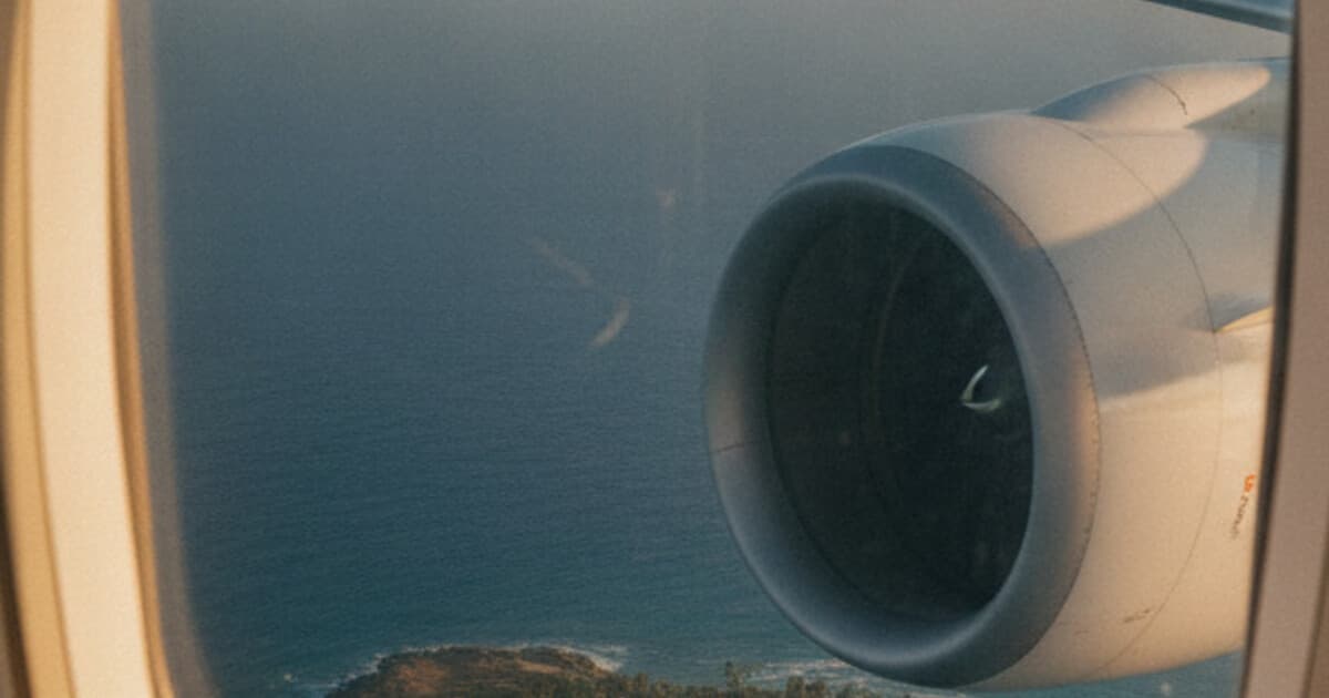 Airliner wing over the sea at sunset seen through a cabin window