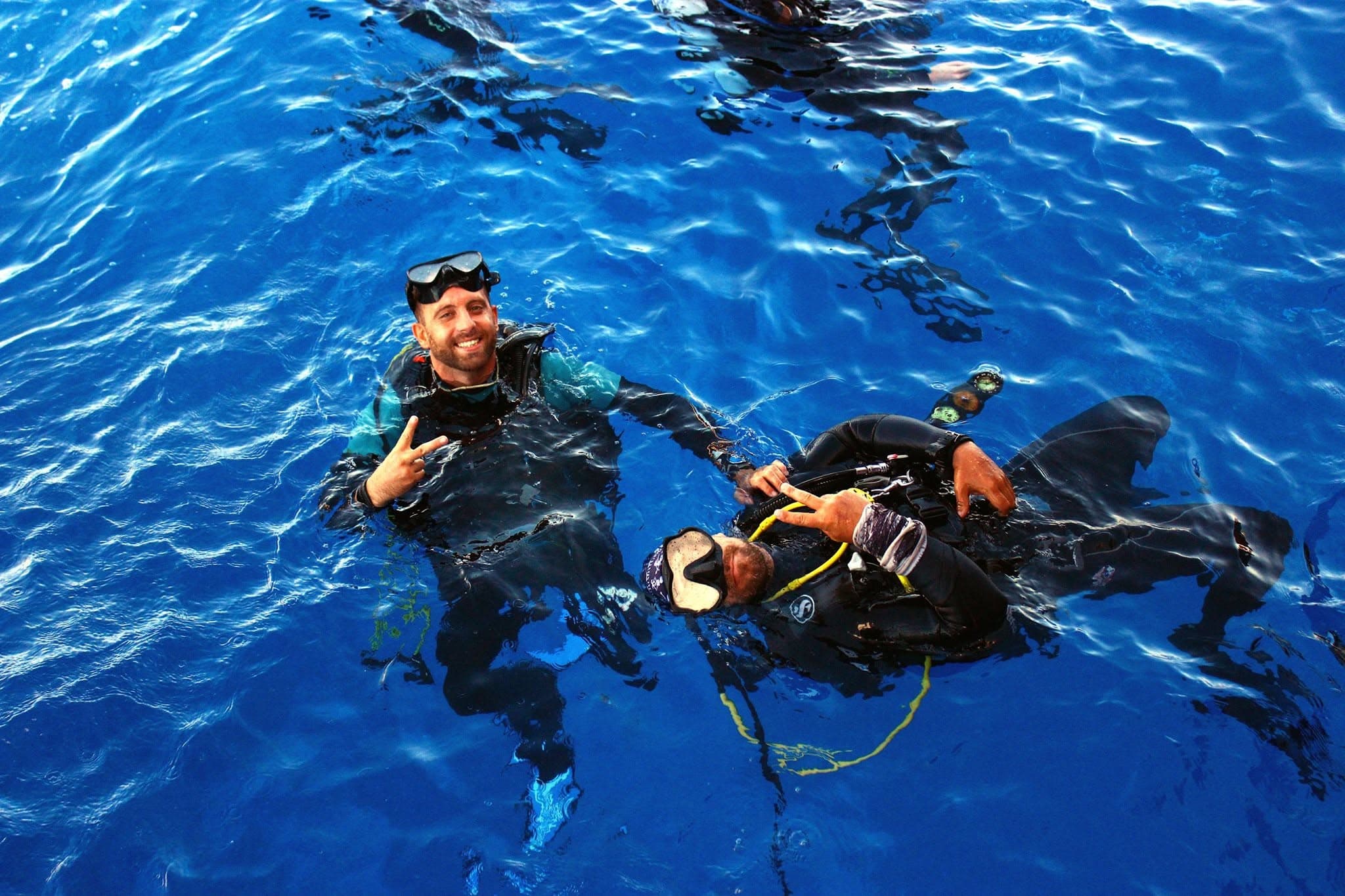 Two dive instructors in the sea, smiling and flashing peace signs at the camera