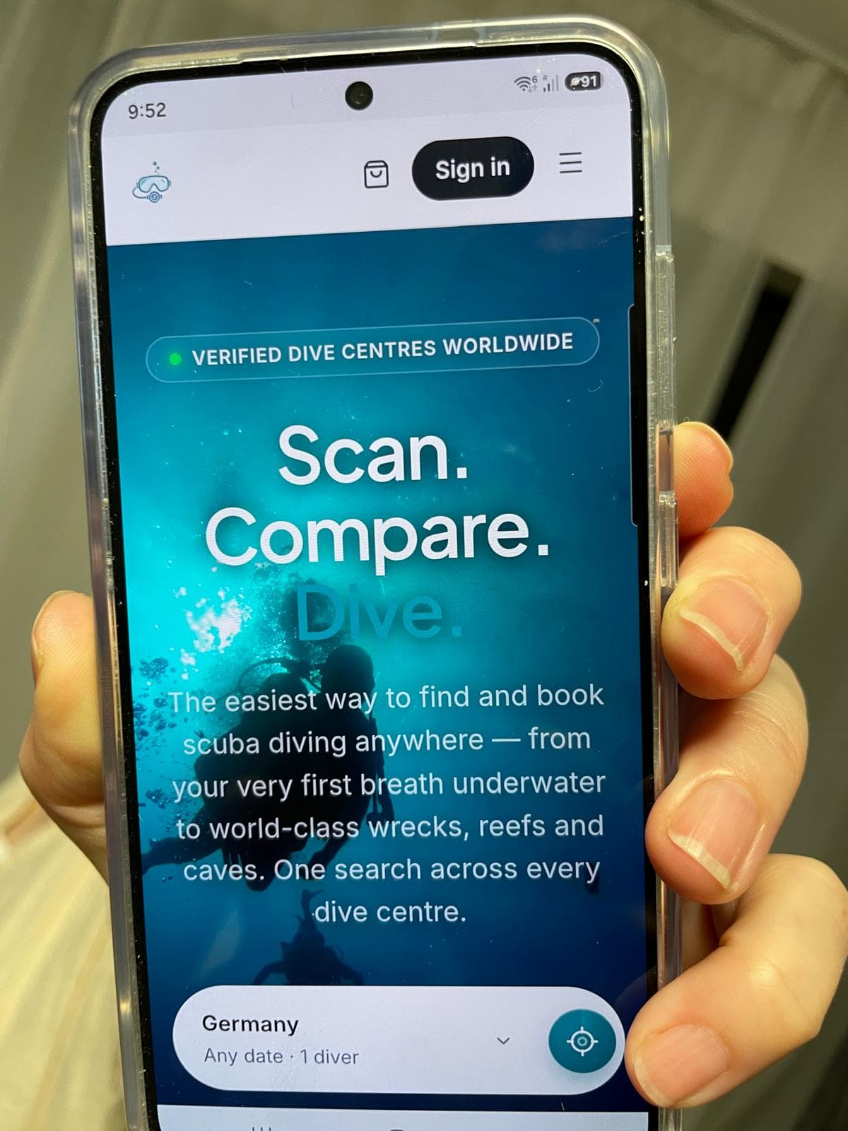 A hand holding a phone showing the live Diving Scanner homepage